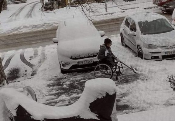 Un bărbat în scaun cu rotile a ieșit, cu lopata, să dea zăpada de pe trotuar